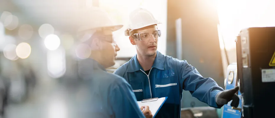 Two engineers in hard hats and safety glasses consulting on production floor