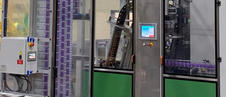 Sleeve labeling machine applying labels to purple bottles on conveyor