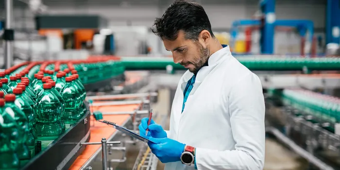 Quality control engineer inspecting sleeve labeling production line with green bottles